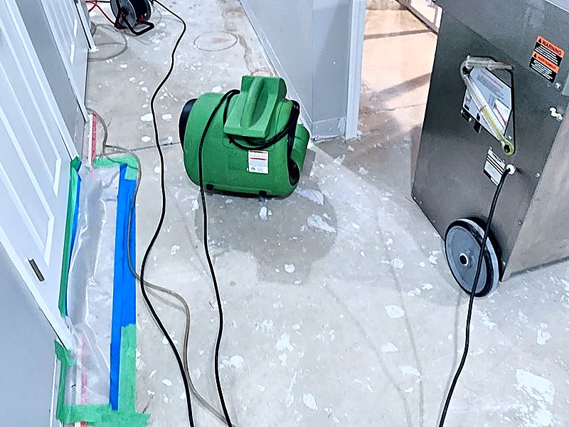Green air movers and a stainless steel dehumidifier set up in a basement hallway with the lower drywall cut out