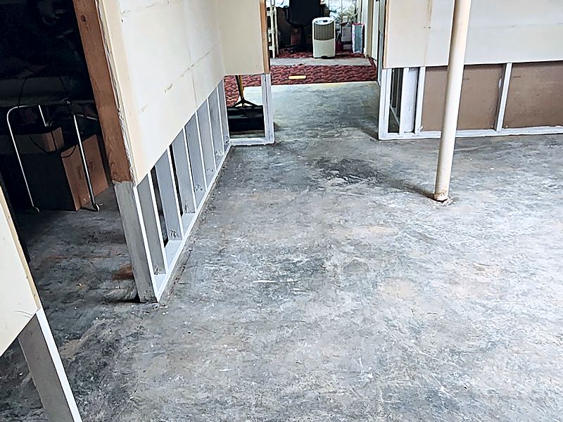 Basement room after a drywall flood cut with the lower section of drywall removed to expose wooden wall studs above a bare concrete floor