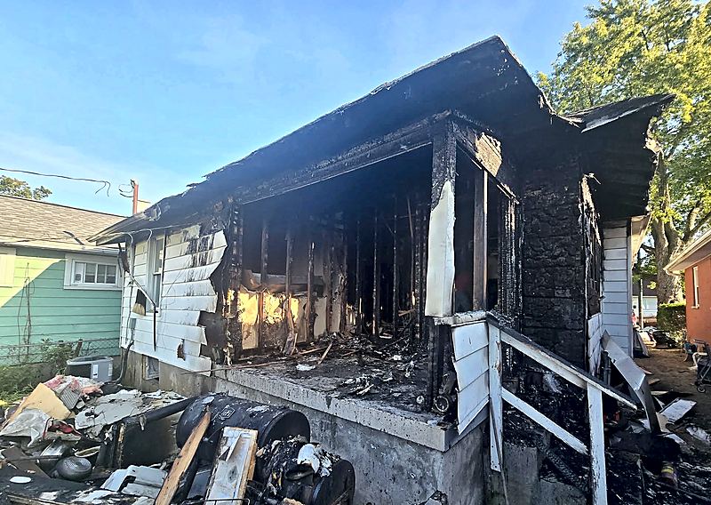 Residential house exterior with severe fire and char damage across the front porch, siding, and roofline